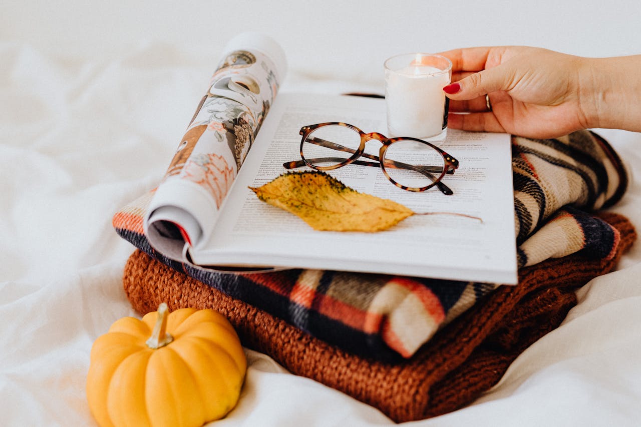 heros-img Close-up of folded fabrics, glasses, candle, and pumpkin for a cozy fall setup.